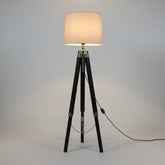 Floor lamp with a beige shade on a tripod base against a gray background